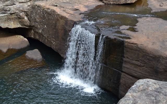 A small waterfall pouring over sandstone into a rock pool in Dharawal National Park