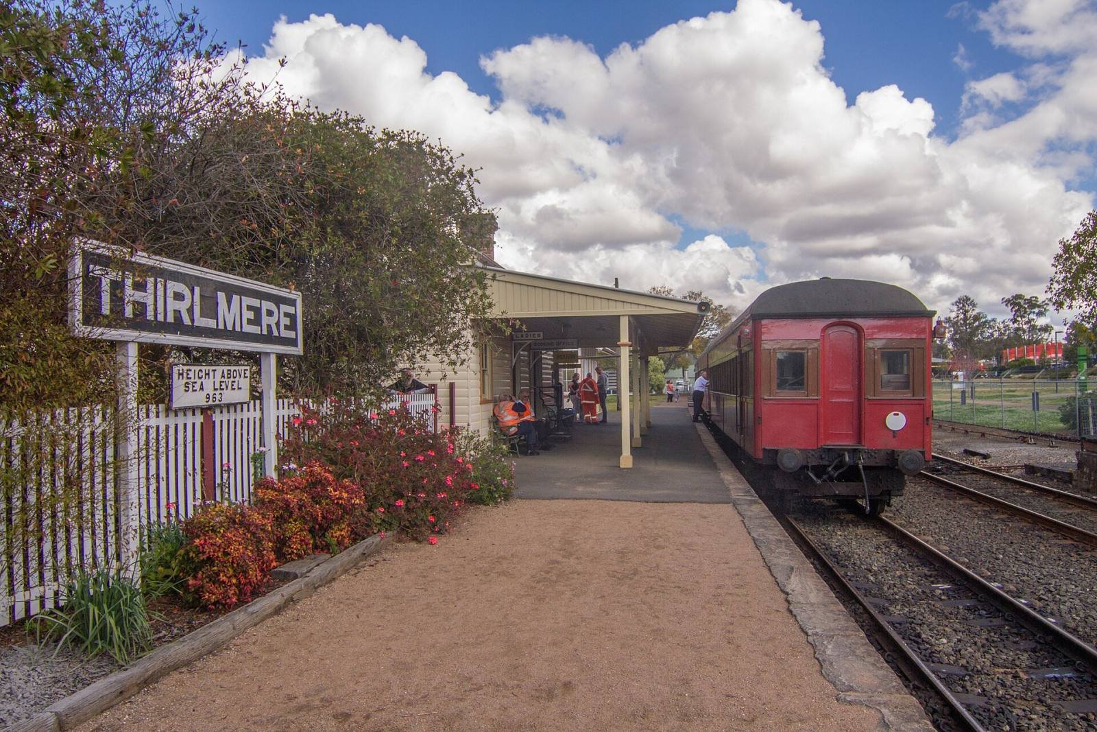 A red heritage carriage at the platform of Thirlmere station beside the station sign