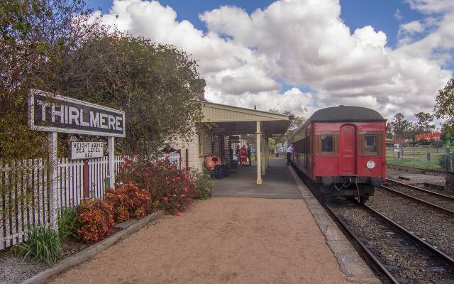 A red heritage carriage at the platform of Thirlmere station beside the station sign