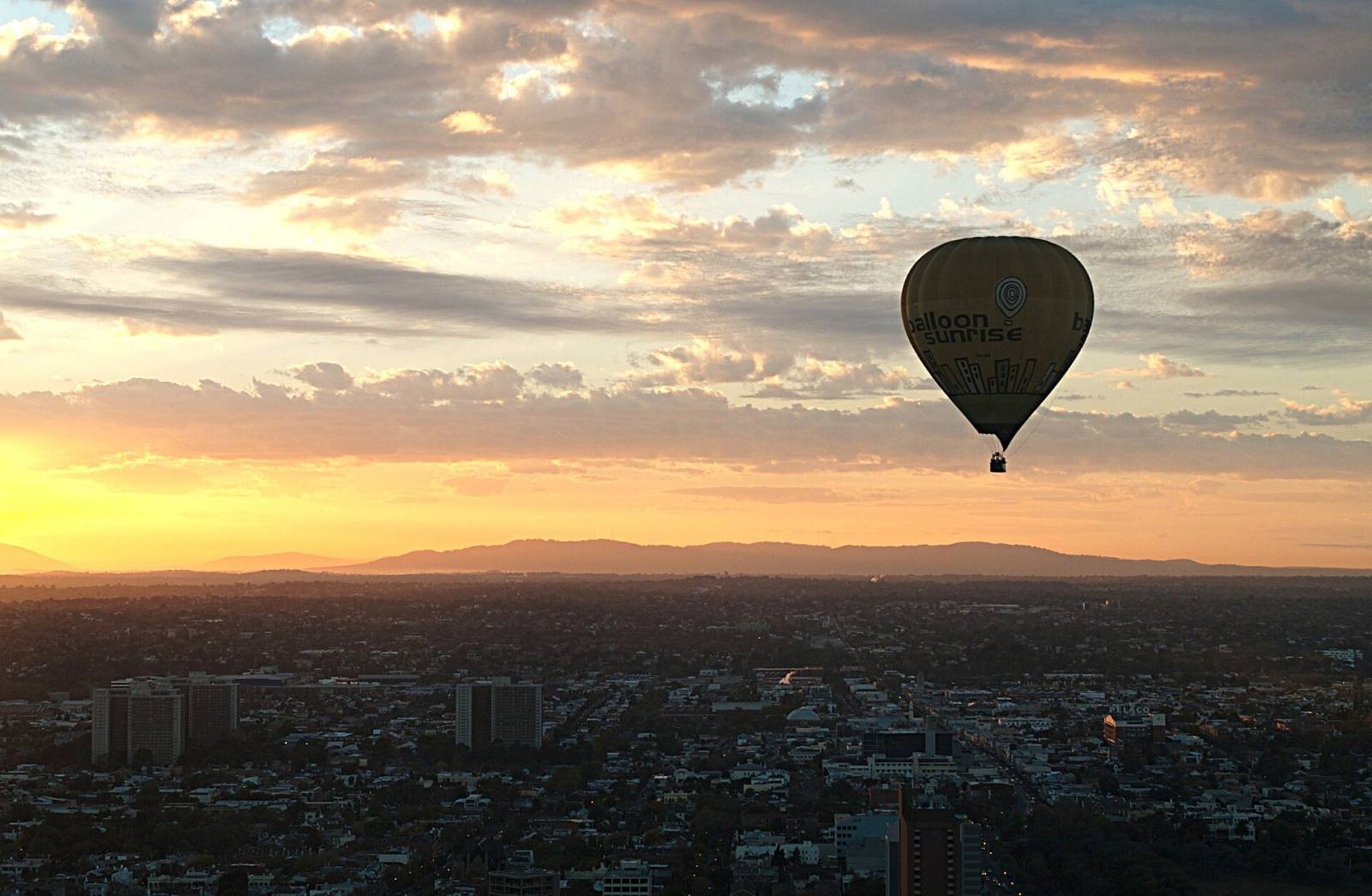 A hot-air balloon floating above a city at sunrise under a golden sky