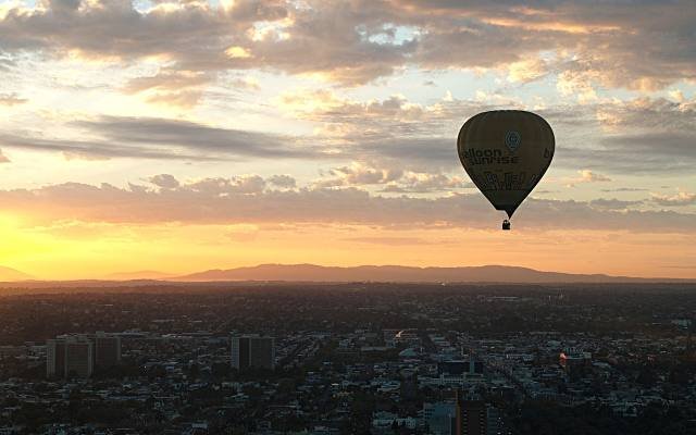 A hot-air balloon floating above a city at sunrise under a golden sky
