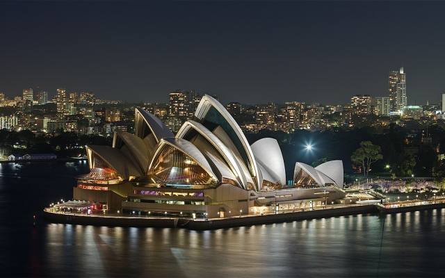 The sails of the Sydney Opera House lit up at night beside the harbour