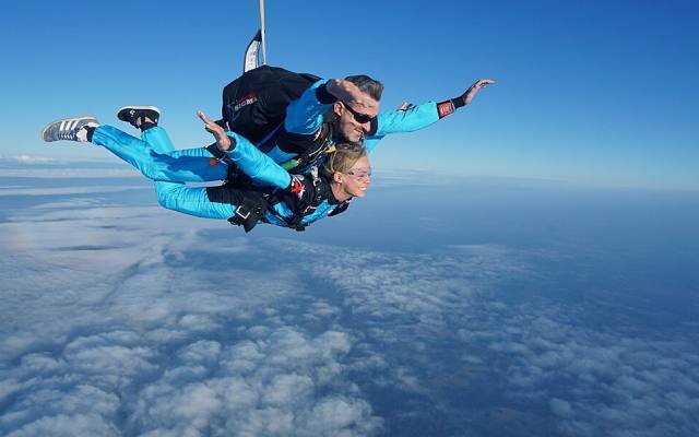 A tandem skydiver and instructor in freefall high above the clouds